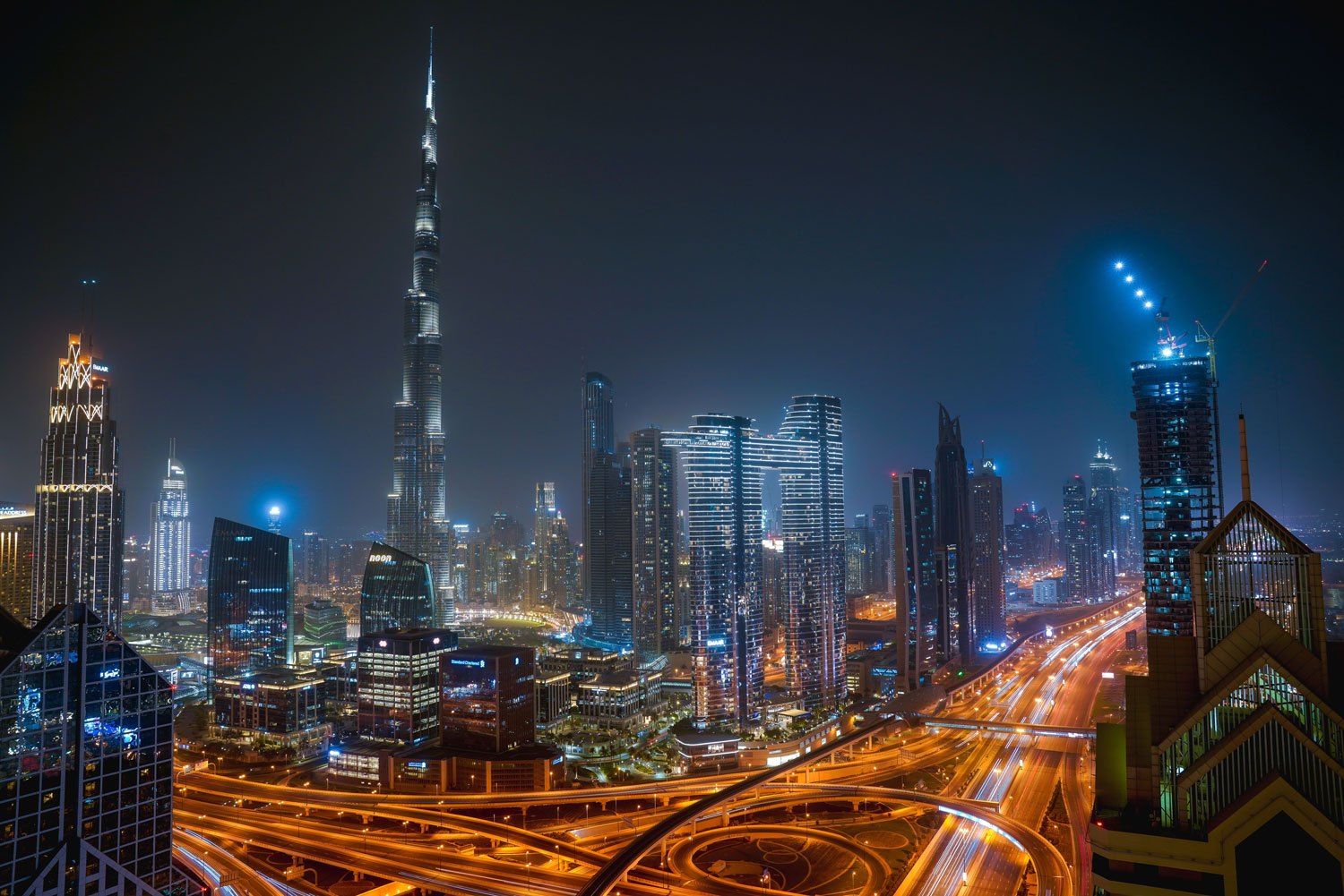 Dubai skyline at night, with the Burj Khalifa above illuminated towers and highway interchanges